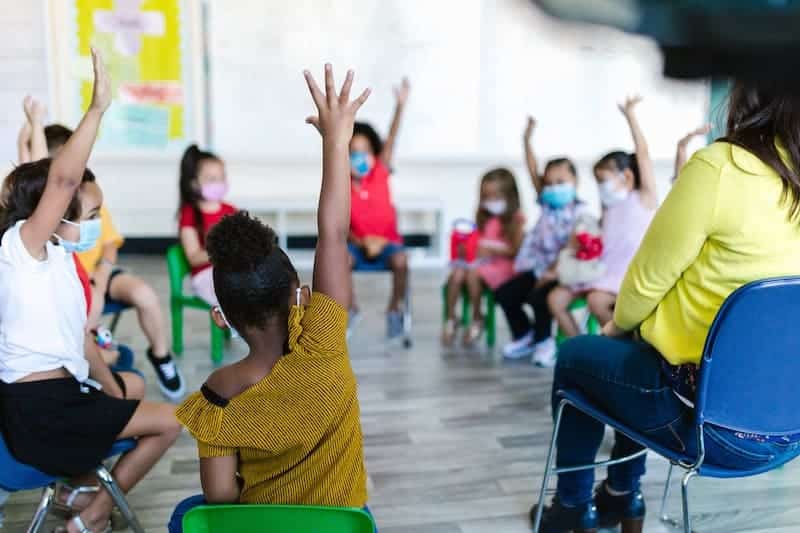 children with hands raised in the classroom