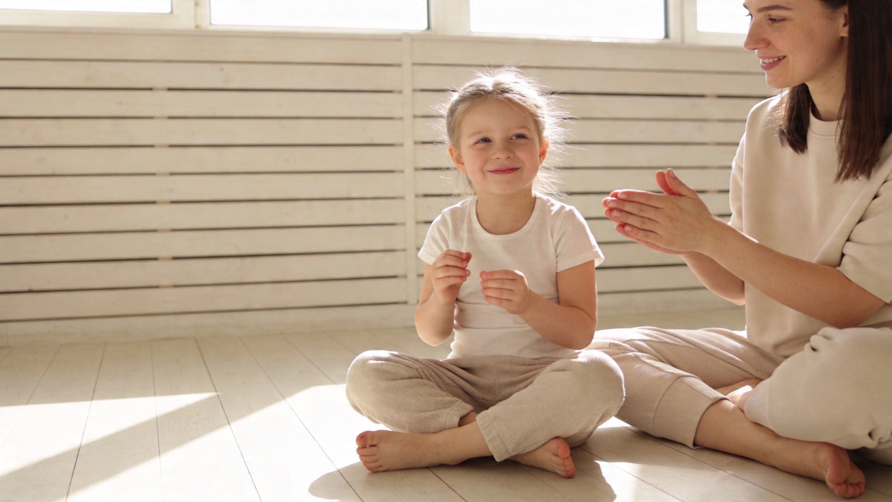 A happy young girl and her mother sitting on the wooden floor and playing together at home.