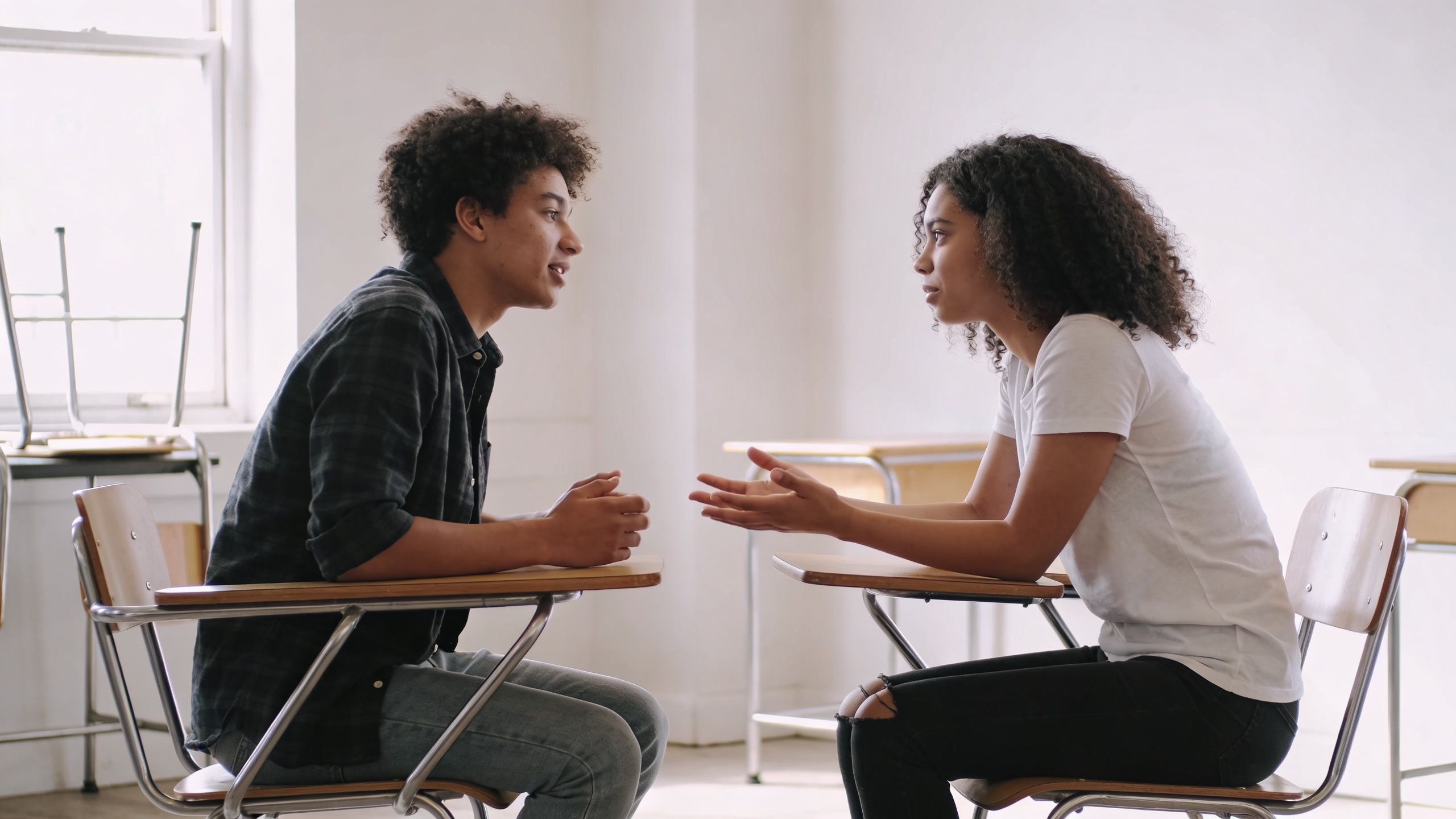 Two students sitting face to face in a classroom engaged in an active conversation.