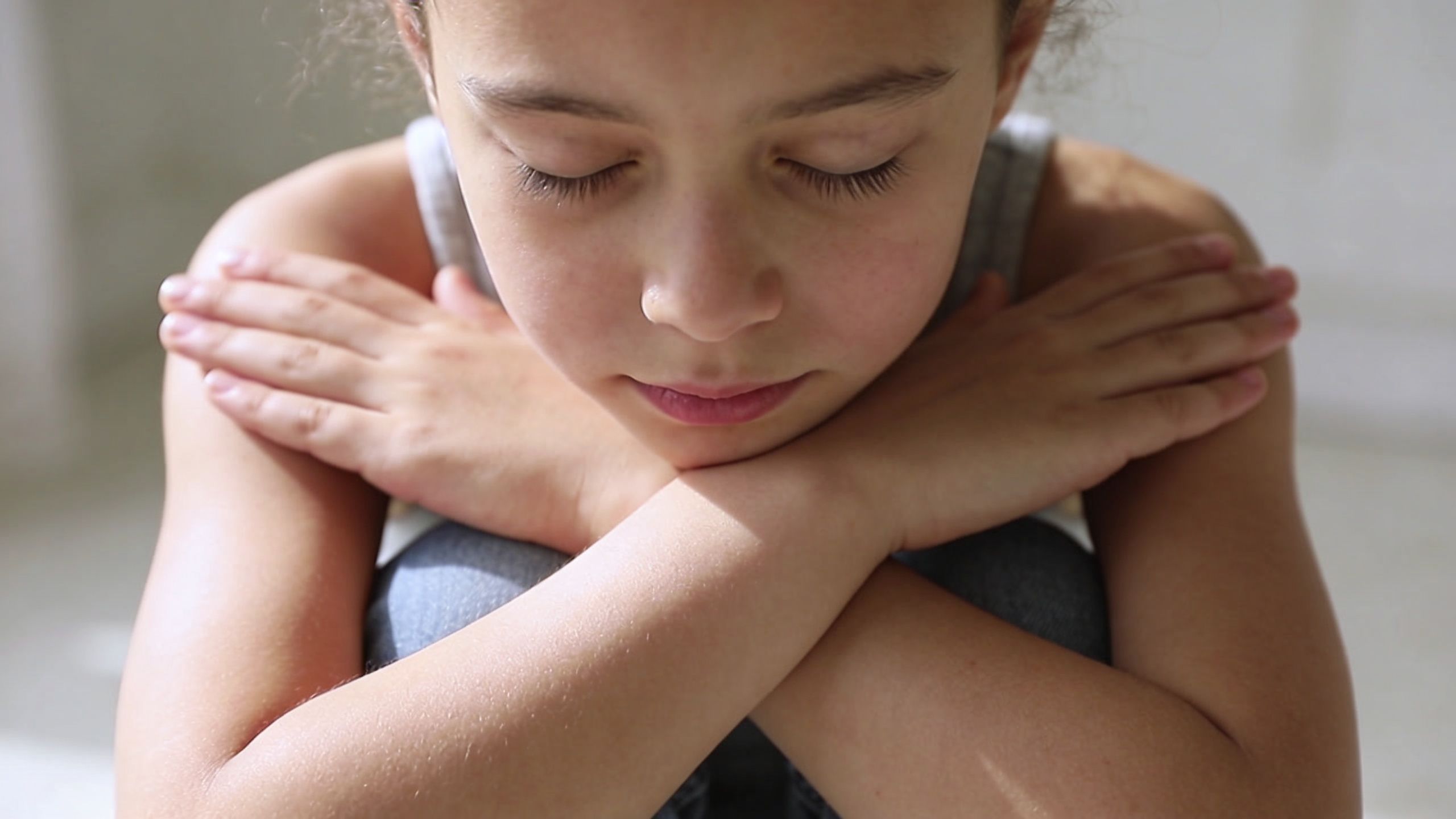 A young girl sitting with her eyes closed and arms crossed, practicing a calming self-hug technique.