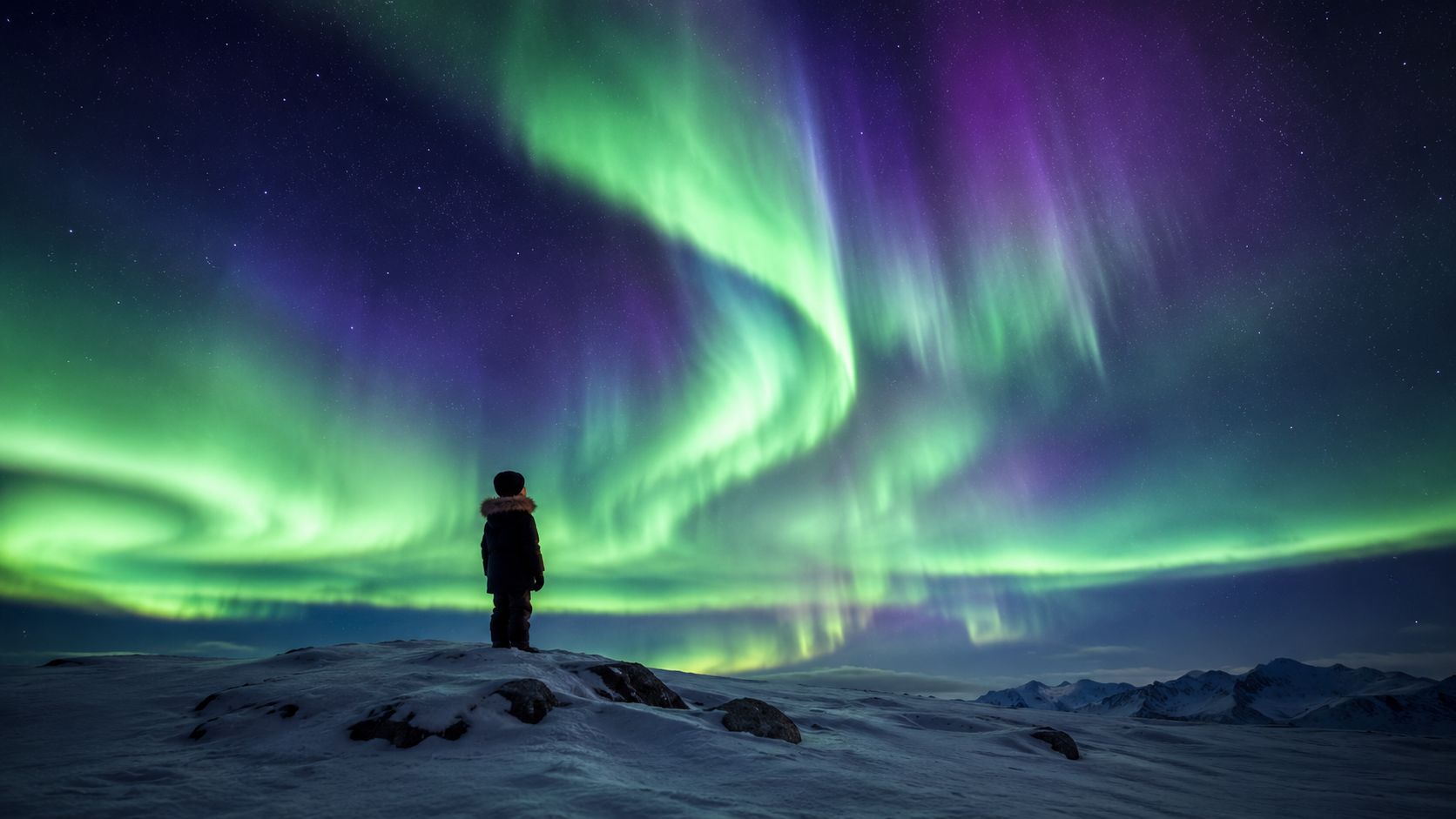 A child in a winter coat stands on a snowy hill, observing the vibrant aurora borealis overhead.