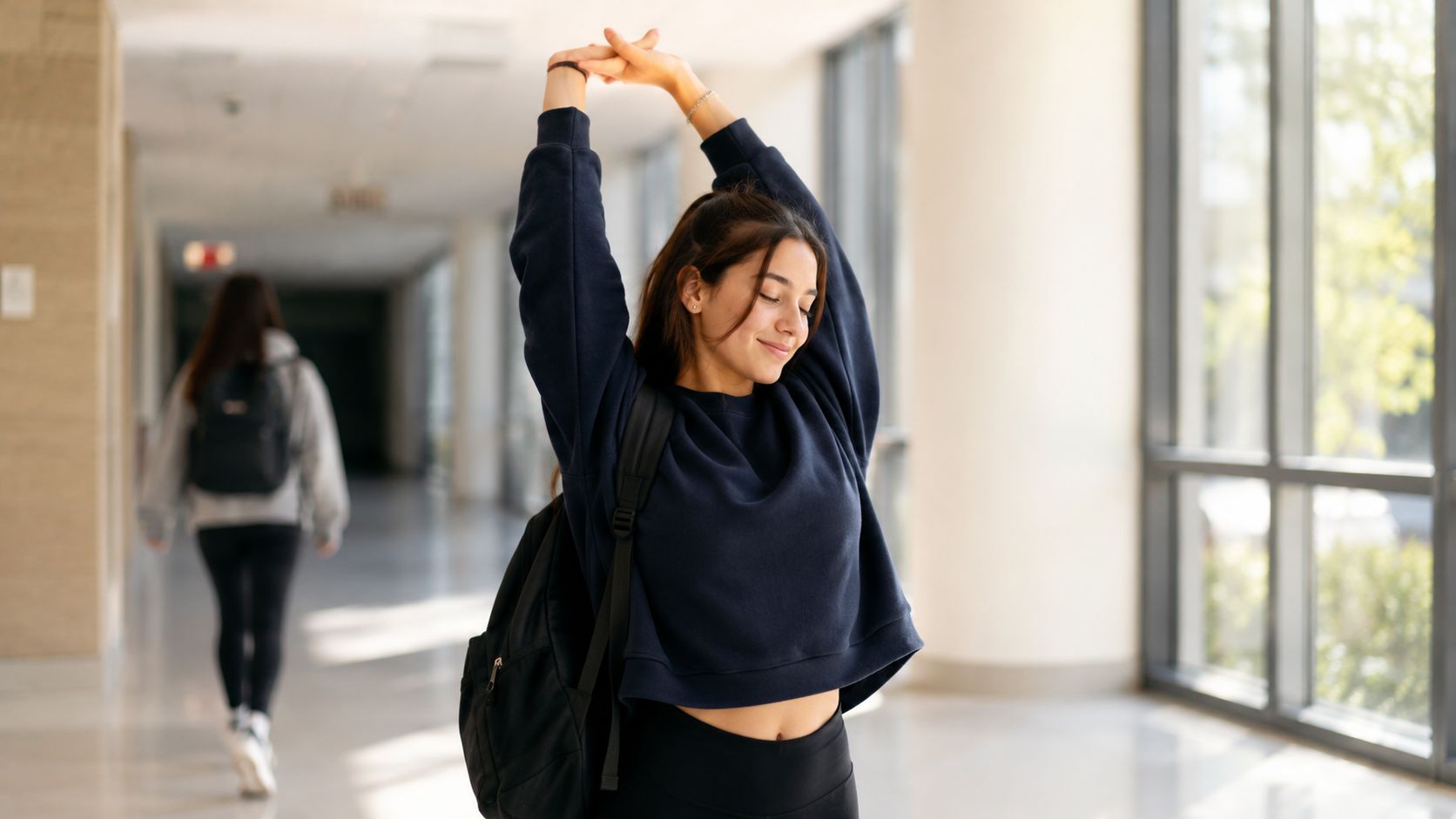 A female college student stretching her arms in a school hallway to relieve stress before exams.