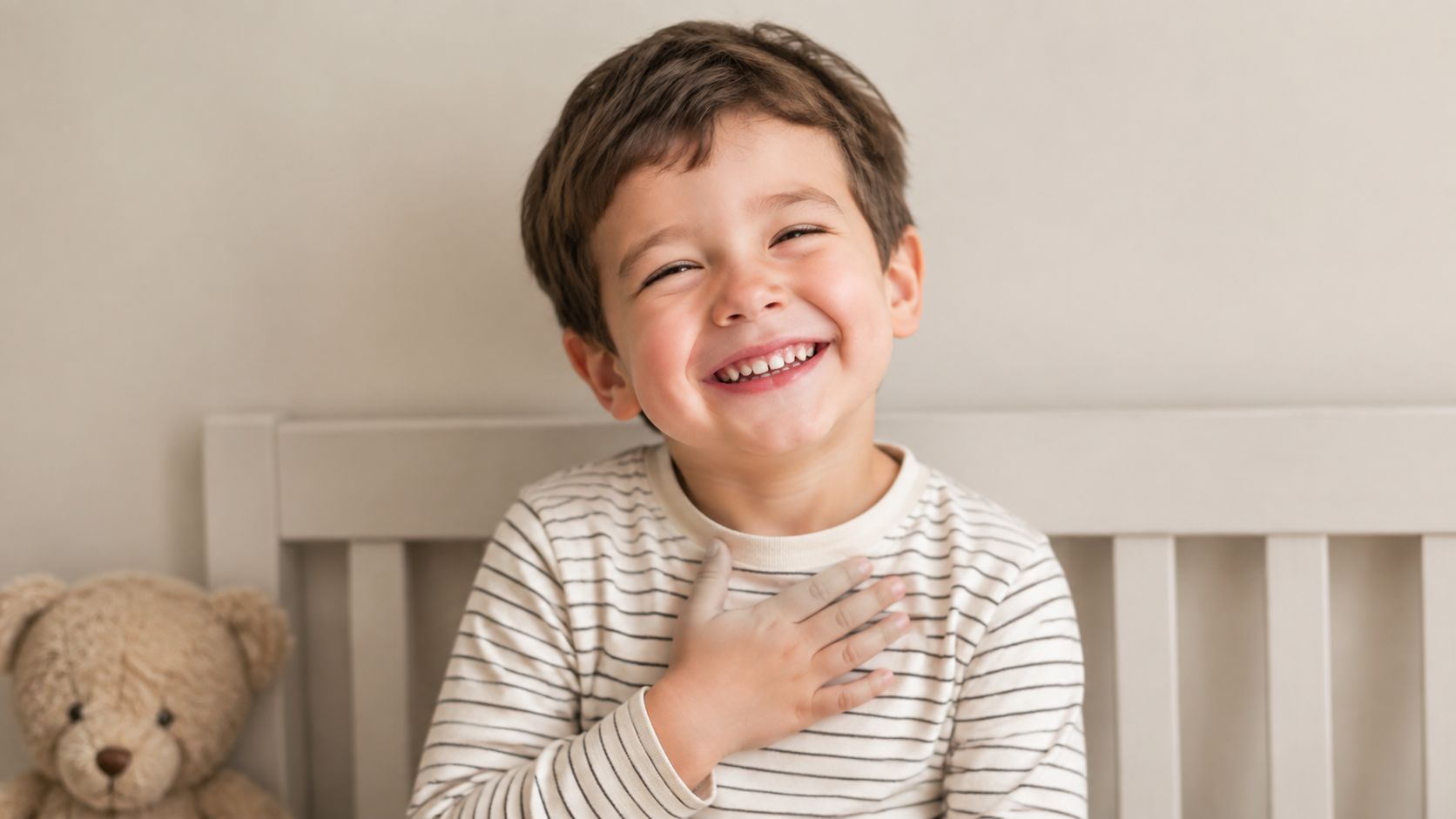 A happy young boy wearing a striped shirt laughing with his hand placed on his chest.